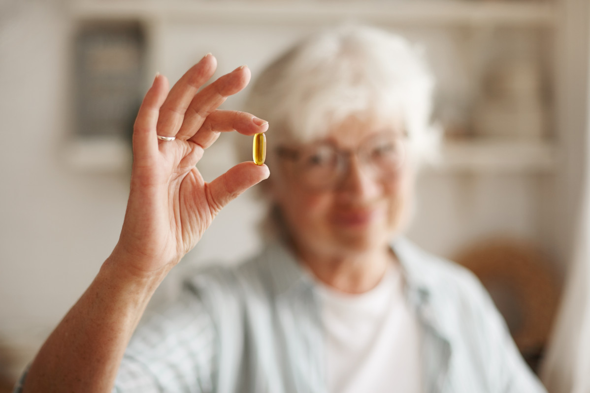 Concepto de alimentacion nutricion dieta y salud primer plano de la mano de una anciana con aceite de pescado o suplemento de acidos grasos poliinsaturados omega 3 en forma de capsula que va tomar uno durante el almuerzo